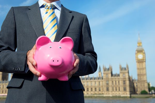 A suited man holding a piggy bank outside UK parliament